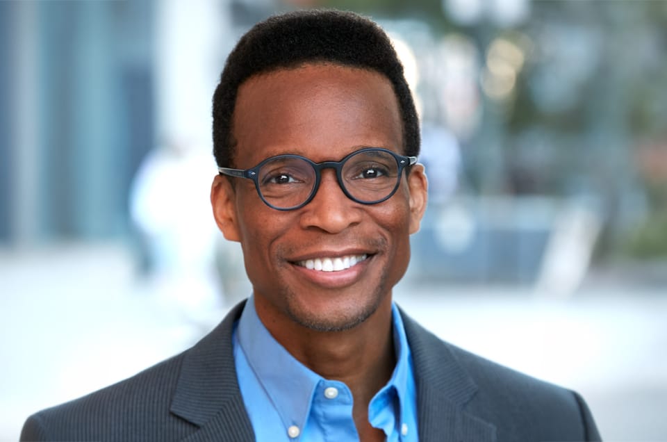 Professional commercial headshot of a smiling man wearing glasses and a blue blazer, photographed by Headshots LA