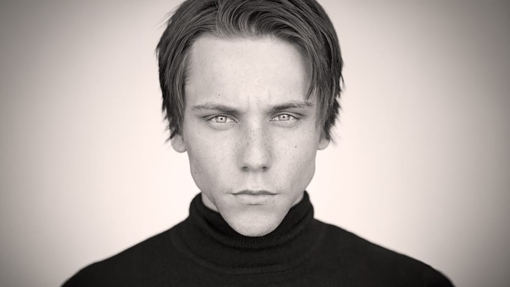 Dramatic black-and-white acting headshot of actor James Austin Kerr with tousled blond hair, wearing a black turtleneck against a soft gray background.