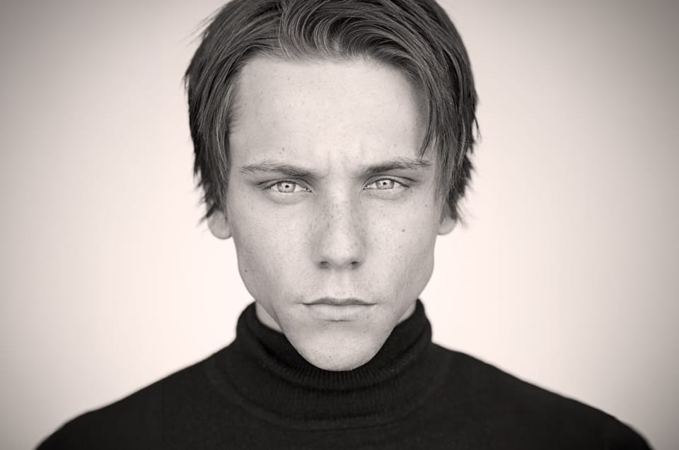 Dramatic black-and-white acting headshot of actor James Austin Kerr with tousled blond hair, wearing a black turtleneck against a soft gray background.