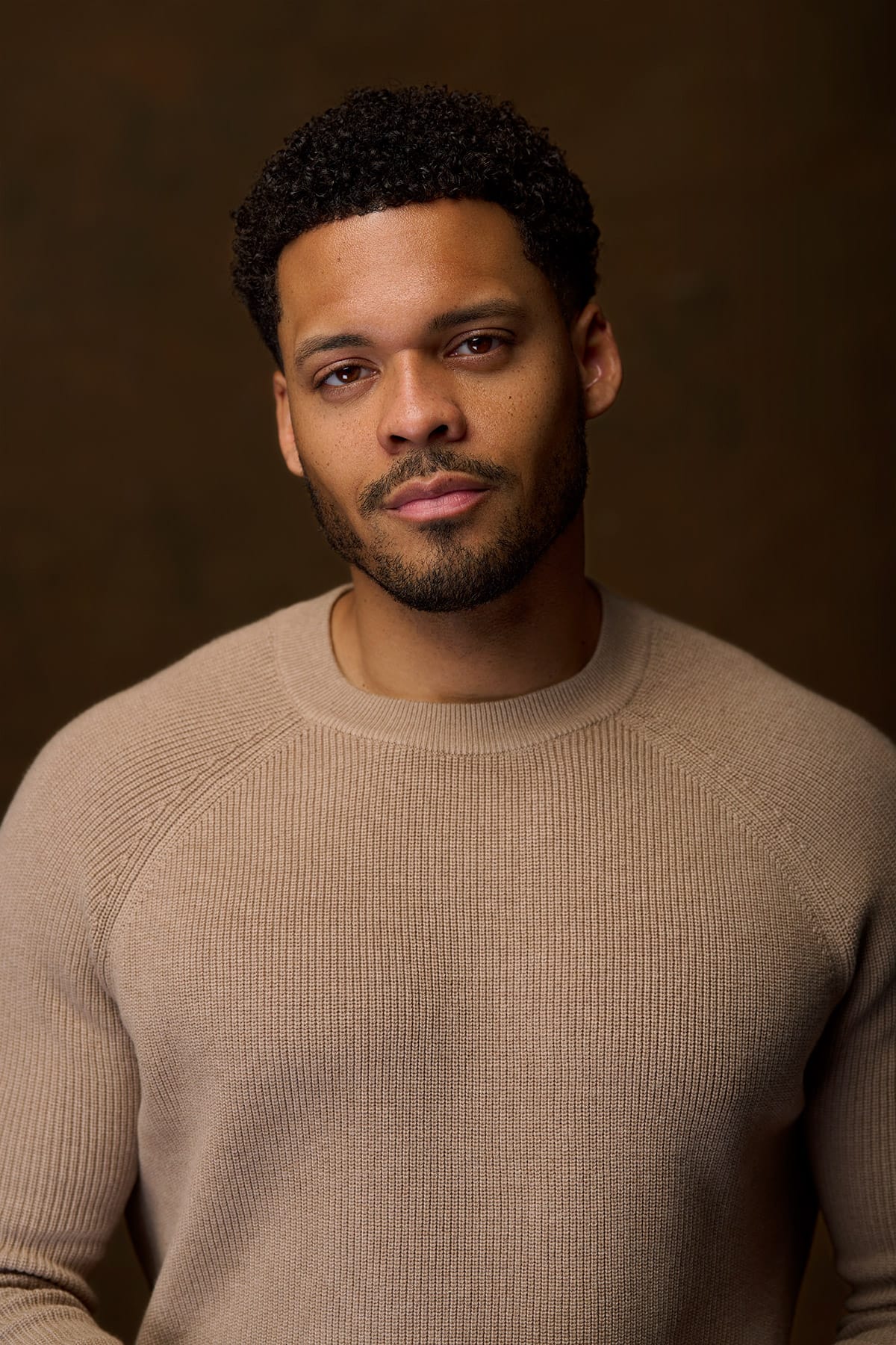 Deric Augustine in a taupe ribbed sweater on a warm brown backdrop — celebrity headshot by Headshots LA in Los Angeles.