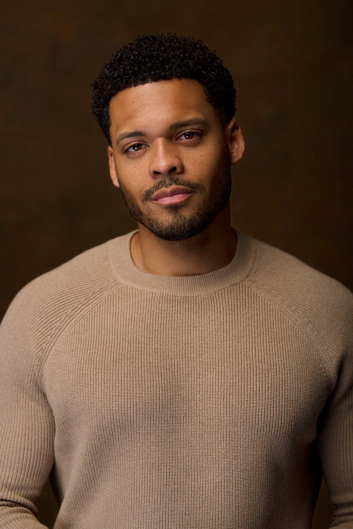Deric Augustine in a taupe ribbed sweater on a warm brown backdrop - celebrity headshot by Headshots LA in Los Angeles.