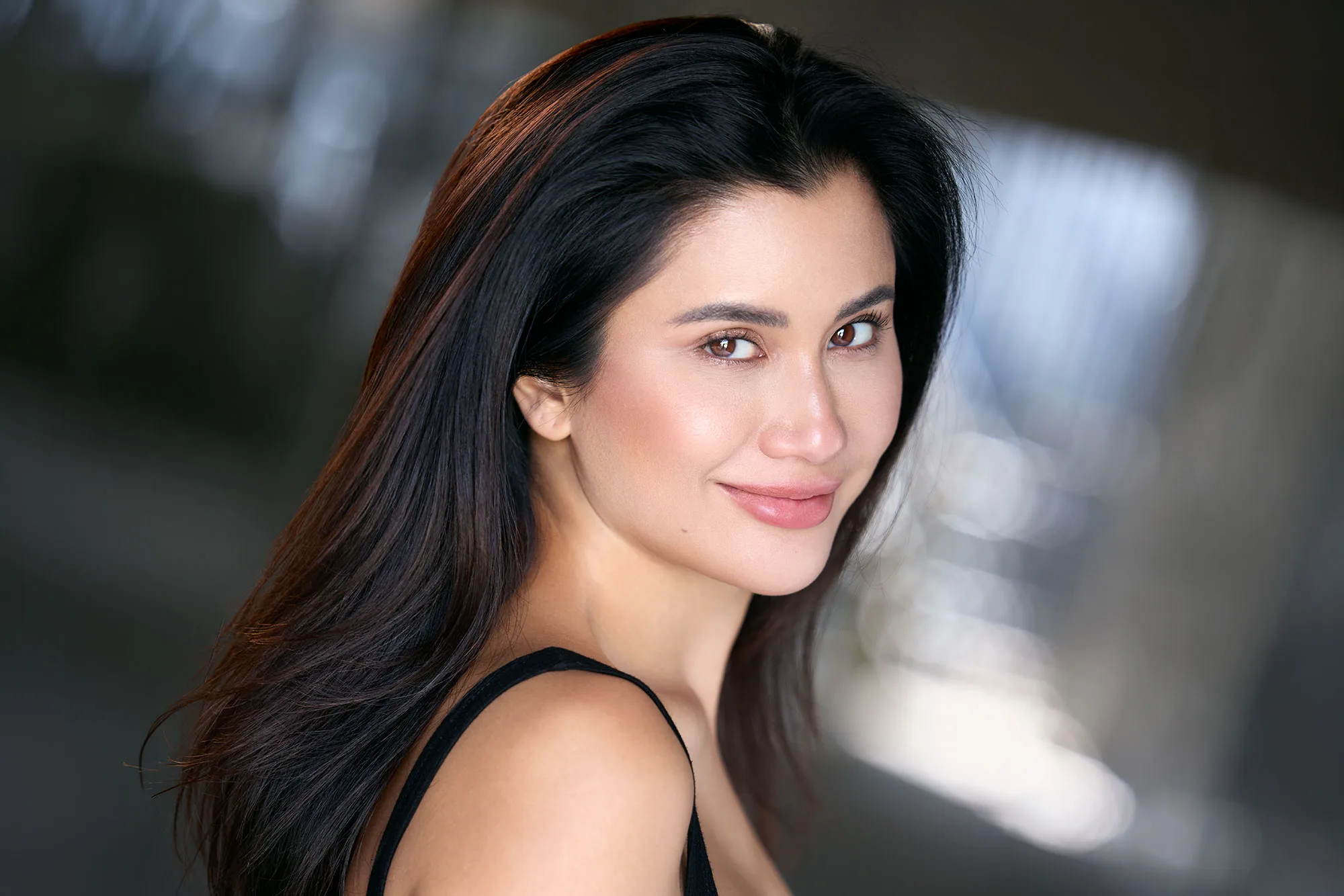 Praya Lundberg with long dark hair in a black top against a warm, softly blurred background - celebrity headshot by Headshots LA in Los Angeles.