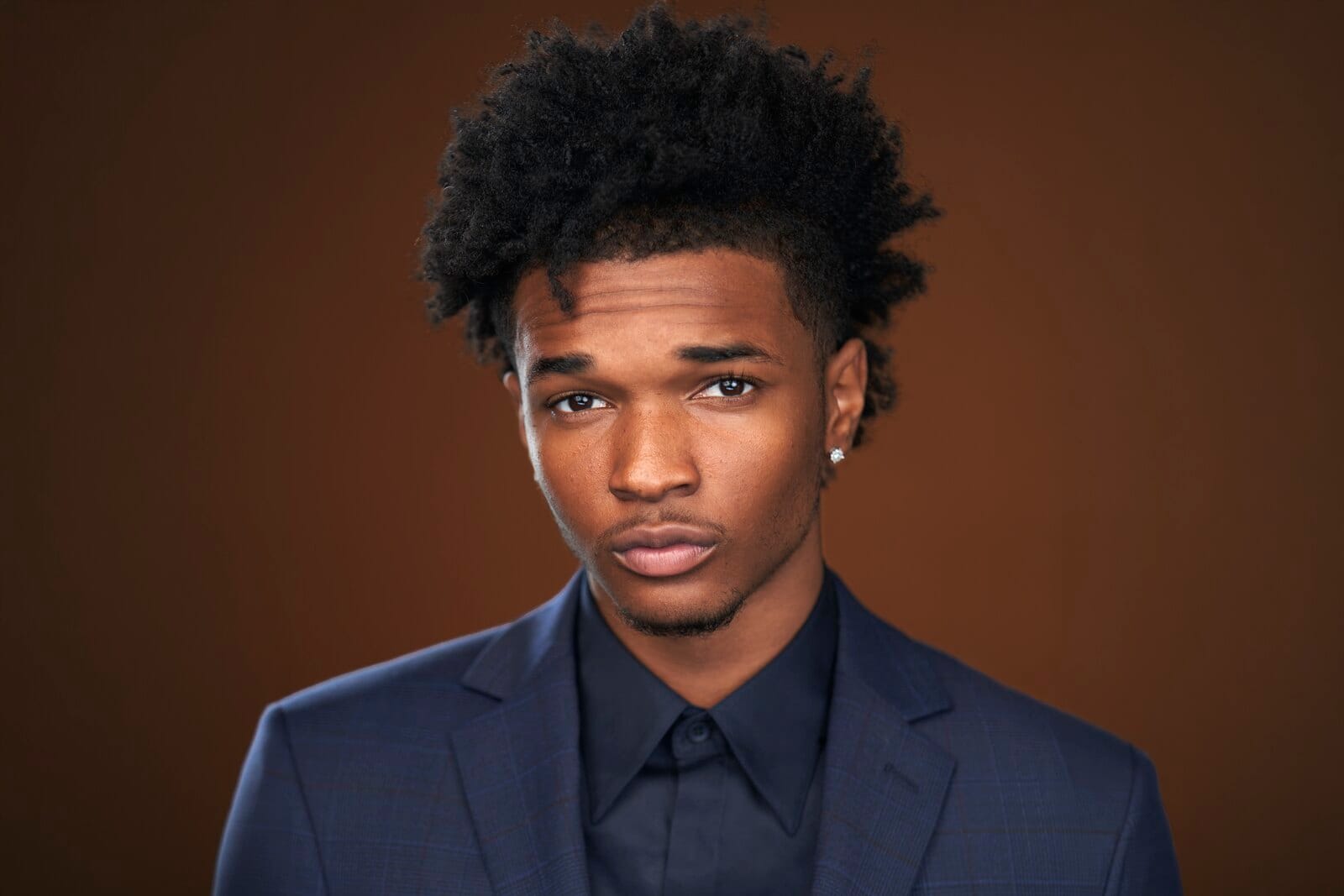 Isaiah Hill in a navy plaid suit on a warm brown backdrop — celebrity headshot by Headshots LA in Los Angeles.